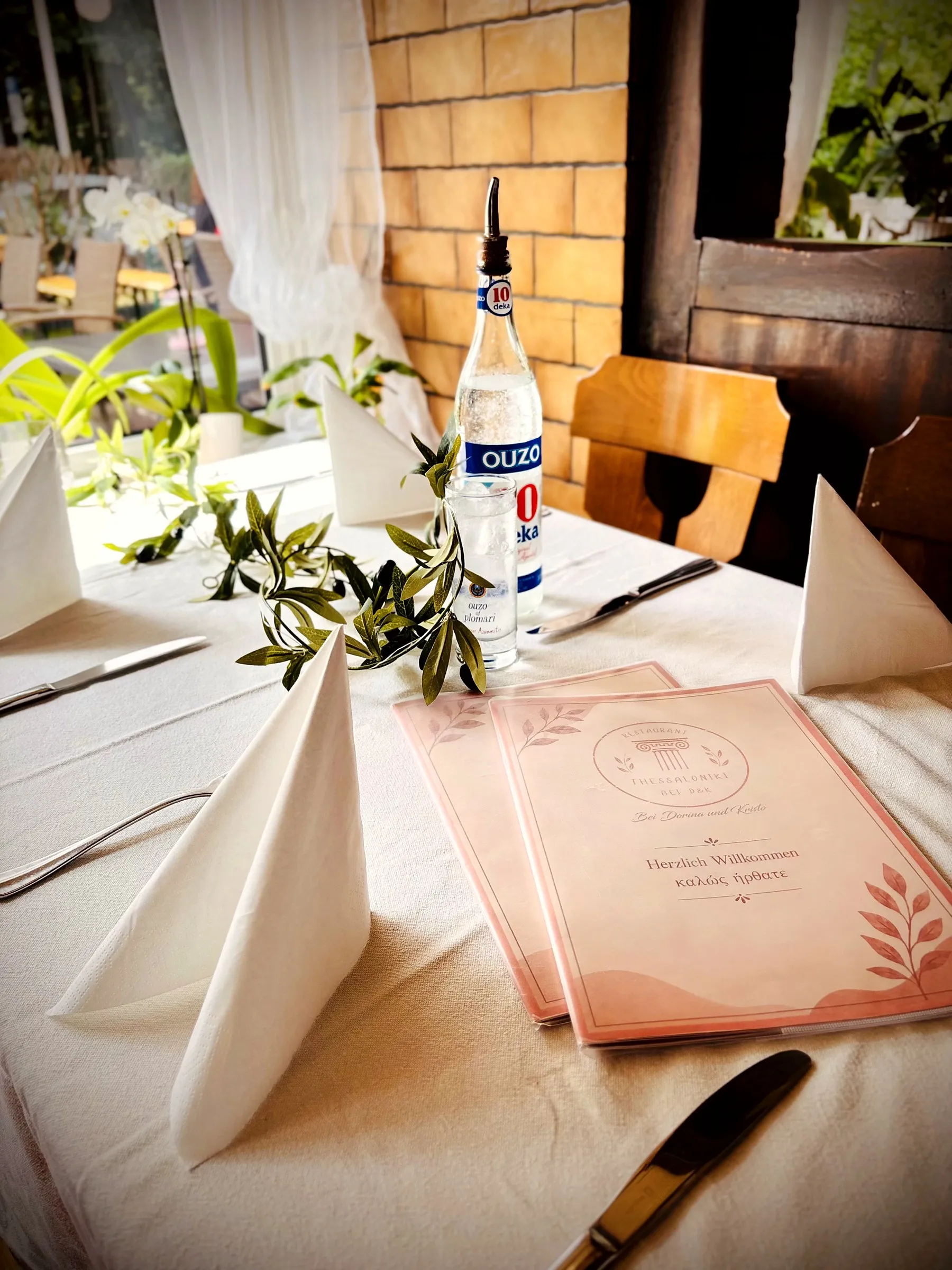 Gedeckter Tisch mit Speisekarte, Ouzo und einem Olivenzweig